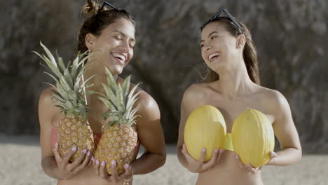 Front-view-of-smiling-women-with-pineapples-and-melons-on-beach